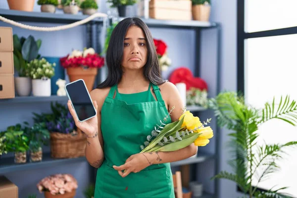 Brunette woman working at florist shop holding smartphone depressed and worry for distress, crying angry and afraid. sad expression.