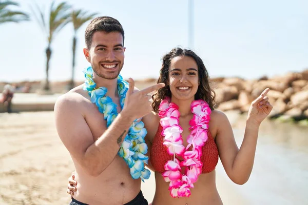若いですヒスパニック系のカップル身に着けていますHawaiianネックレスでザビーチ笑顔幸せなポインティングとともに手と指 — ストック写真