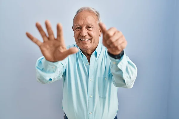 Starší Muž Šedými Vlasy Stojící Nad Modrým Pozadím Ukazuje Ukazuje — Stock fotografie