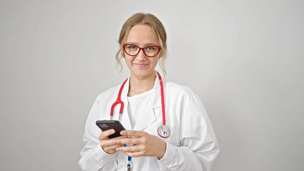 年轻的金发女医生在孤独的白色背景下 用智能手机微笑 — 图库照片