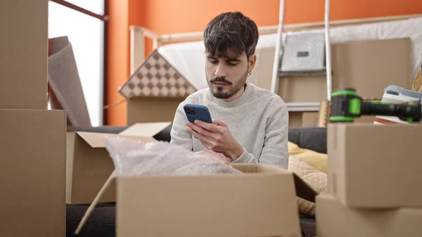 Junger Hispanischer Mann Packt Pappschachtel Mit Smartphone Neuen Zuhause Aus — Stockfoto
