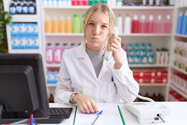 Молодая Белая Женщина Работающая Аптеке Разговаривает Телефону Надувая Щеки Смешным — стоковое фото