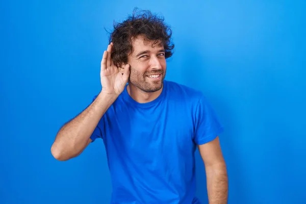 Іспанський Молодий Чоловік Стоїть Над Синім Фоном Усміхаючись Рукою Вухом — стокове фото