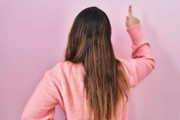 Молода Іспаномовна Жінка Стоїть Над Рожевим Тлом Позуючи Назад Вказуючи — стокове фото