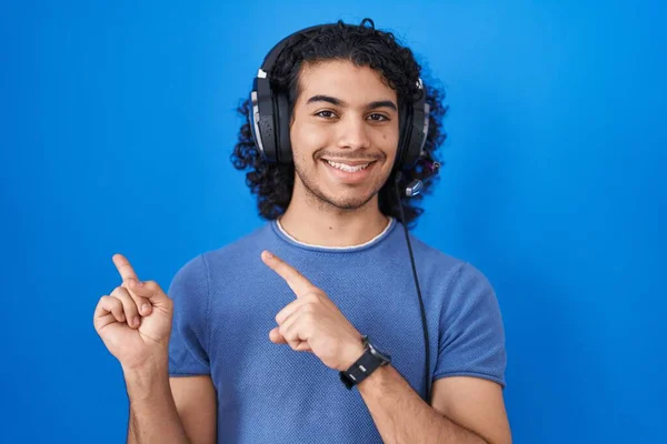 西班牙裔男人 一边听音乐一边用耳机微笑 一边用双手和手指看着摄像机 — 图库照片