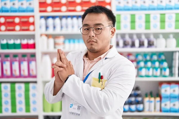 Chinese young man working at pharmacy drugstore holding symbolic gun with hand gesture, playing killing shooting weapons, angry face