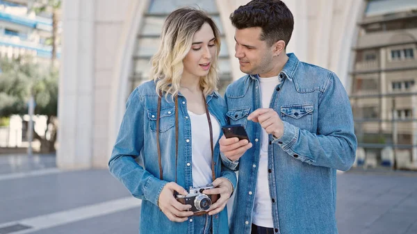 男性と女性のカップルが一緒に路上でスマートフォンを使用して立って — ストック写真
