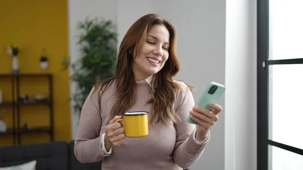 Young Beautiful Hispanic Woman Using Smartphone Drinking Coffee Home — Fotografia de Stock
