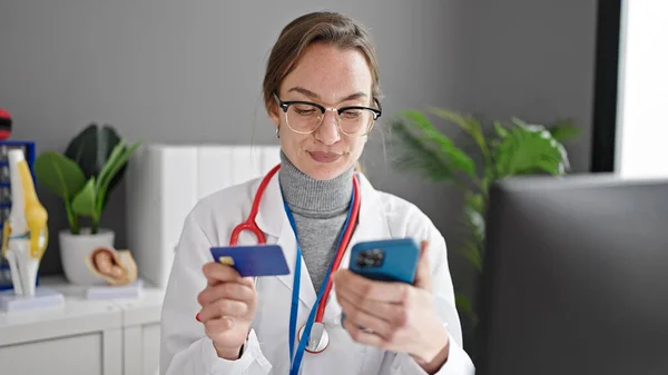 年轻的高加索女医生在诊所用智能手机和信用卡购物 — 图库照片