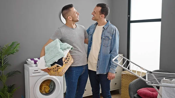 二人の男は 洗濯室で服を着て自信を持って保持バスケット笑顔 — ストック写真