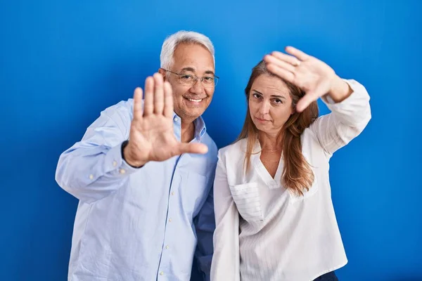 中世のヒスパニック系のカップルが青い背景に立って手の手のひらと指を使用してフレームを行う カメラの視点 — ストック写真
