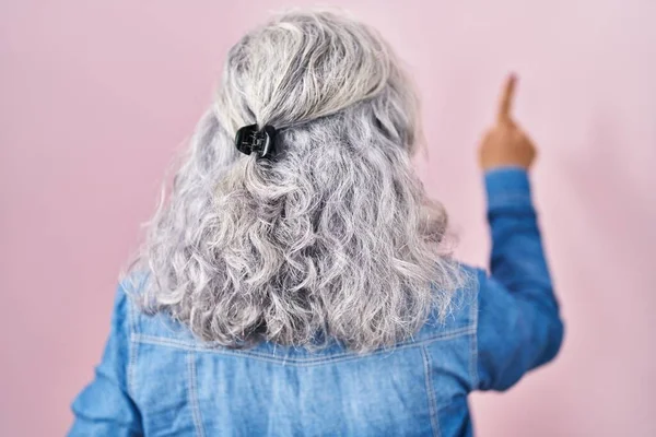 中年妇女 灰头发 站在粉红的背景上 背对背 手指头指向前方 — 图库照片