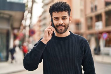 Genç Arap adam gülümsüyor, kendinden emin bir şekilde caddedeki akıllı telefondan konuşuyor.