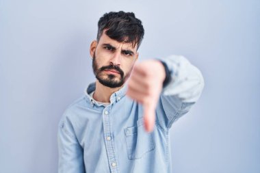 Mavi arka planda sakallı, mutsuz ve kızgın görünen, reddedilmiş ve olumsuz davranışlı genç İspanyol bir adam. kötü ifade. 