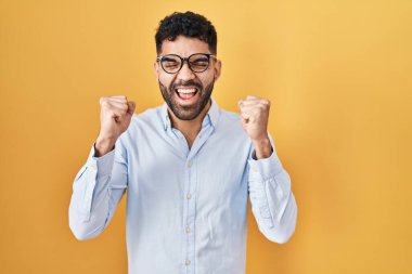 Sarı arka planda duran İspanyol sakallı adam kolları havada ve gözleri kapalı zaferi kutlarken heyecanla bekliyor. Kazanan konsept. 