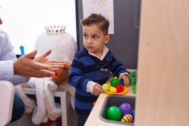 Adorable hispanic boy playing with play kitchen standing at kindergarten