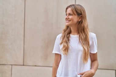 Young blonde girl smiling confident looking to the side over white isolated background