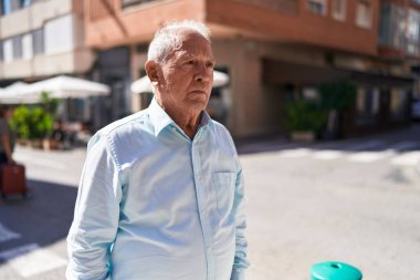 Middle age grey-haired man looking to the side with serious expression at street