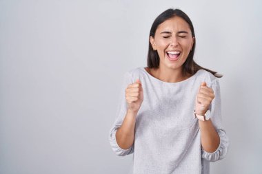 Beyaz arka planda duran genç İspanyol kadın başarı için heyecanlı kolları havada ve gözleri kapalı zaferi kutlarken gülümsüyor. Kazanan konsept. 