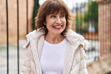 Orta yaşlı bir kadın sokakta kendinden emin bir şekilde gülümsüyor.