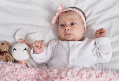 Adorable caucasian baby lying on bed with dolls at bedroom