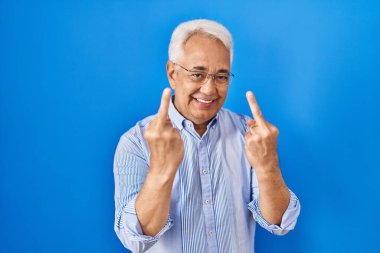 Hispanic senior man wearing glasses showing middle finger doing fuck you bad expression, provocation and rude attitude. screaming excited 