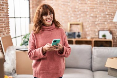 Middle age woman smiling confident using smartphone at new home