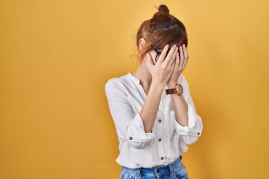 Sarı arka plan üzerine gündelik tişört giyen genç ve güzel bir kadın. Ağlarken suratını ellerle kapatan üzgün bir ifade. depresyon kavramı. 