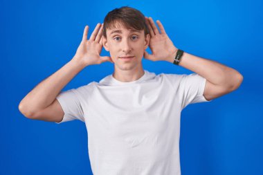 Beyaz, sarışın bir adam mavi arka planda dikilmiş iki elini de kulak hareketi yaparken duymaya çalışıyor. Dedikoduya meraklı. İşitme sorunu, sağır 