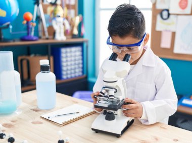 Laboratuvar sınıfında mikroskop kullanan sevimli İspanyol çocuk.