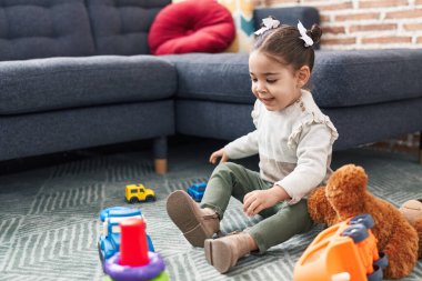 Sevimli İspanyol kız evde yerde oturmuş oyuncaklarla oynuyor.