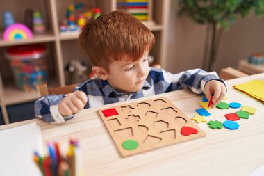 Sınıftaki masada oturan, matematik bilmecesiyle oynayan sevimli çocuk.
