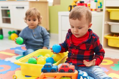 Anaokulunda yerde oturan top ve araba oyuncaklarıyla oynayan sevimli çocuklar.