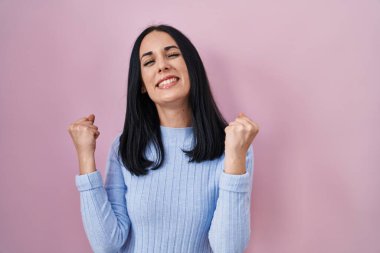 Pembe arka planda duran İspanyol kadın şaşkınlık ve şaşkınlık içinde kollarını kaldırarak ve gözlerini kapayarak başarıyı kutluyor. Kazanan konsept. 