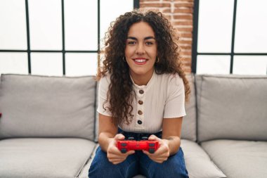 Evdeki kanepede oturmuş video oyunu oynayan genç ve güzel İspanyol kadın.