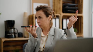 Orta yaşlı İspanyol iş kadını ofisteki akıllı telefondan konuşuyor.