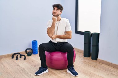 Yoga odasında sakallı İspanyol bir adam elleri çenesinde pilatese oturmuş soru soruyor, düşünceli bir yüz ifadesi var. Düşünceli bir yüzle gülümsüyor. şüphe kavramı. 