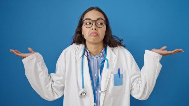 Genç, güzel İspanyol kadın doktor, soyutlanmış mavi arka planda bilgisiz duruyor.