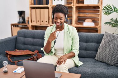 Afrikalı Amerikalı bir kadın danışma ofisinde online seans yapıyor. Mutlu bir şekilde el ve parmak işareti yapıyor. 