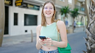 Sokakta akıllı telefon kullanan, kendine güvenen genç sarışın kadın.