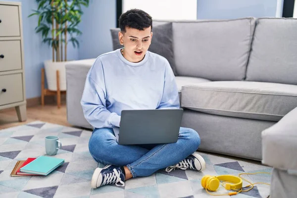 stock image Non binary person studying using computer laptop sitting on the floor afraid and shocked with surprise expression, fear and excited face. 