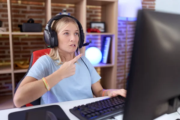 年轻的高加索女人带着耳机玩电子游戏 用食指 关心和惊讶的表情将焦虑和紧张抛在一边 — 图库照片