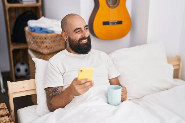 Young Bald Man Using Smartphone Drinking Coffee Bedroom — Stok fotoğraf