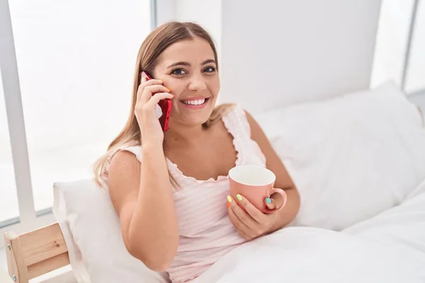 年轻美丽的惊慌失措的女人在卧室里用智能手机喝咖啡 — 图库照片