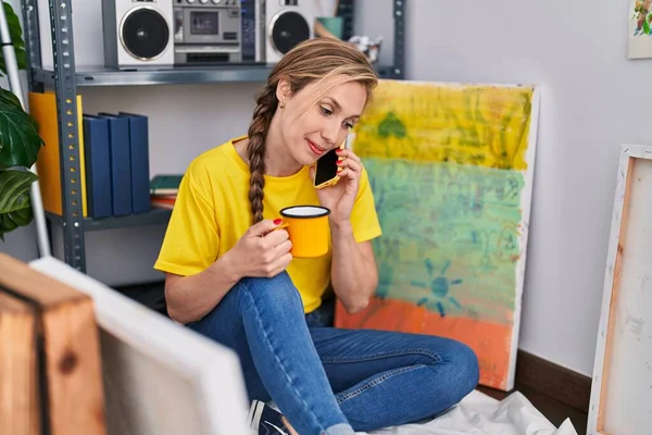 Young Blonde Woman Artist Talking Smartphone Drinking Coffee Art Studio — Foto Stock