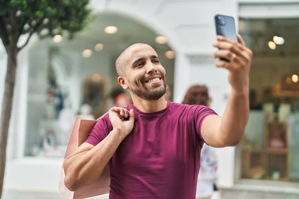 年轻的拉丁男人拿着购物袋在街上用智能手机自制 — 图库照片