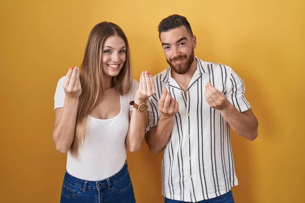 Young Couple Standing Yellow Background Doing Money Gesture Hands Asking — Stock Photo, Image