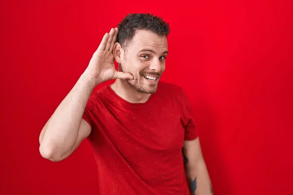 Young Hispanic Man Standing Red Background Smiling Hand Ear Listening — Stock Photo, Image