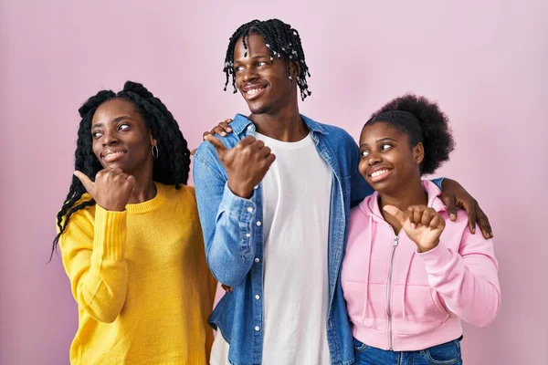 一组三个年轻的黑人站在粉红的背景上 面带微笑 面带微笑 手指头指向一边 — 图库照片