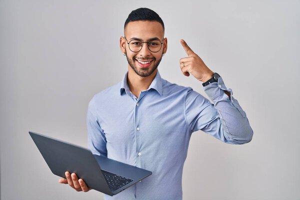 Young hispanic man working using computer laptop smiling amazed and surprised and pointing up with fingers and raised arms. 